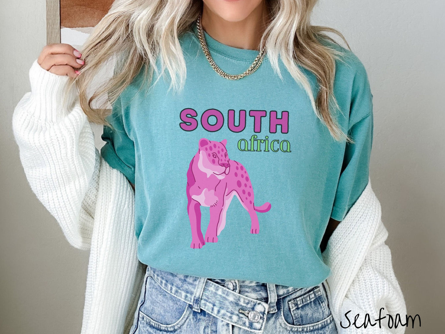 A woman wearing a vintage, seafoam colored shirt with the text South Africa in pink and green font, respectively, and a pink tiger underneath on the prowl.