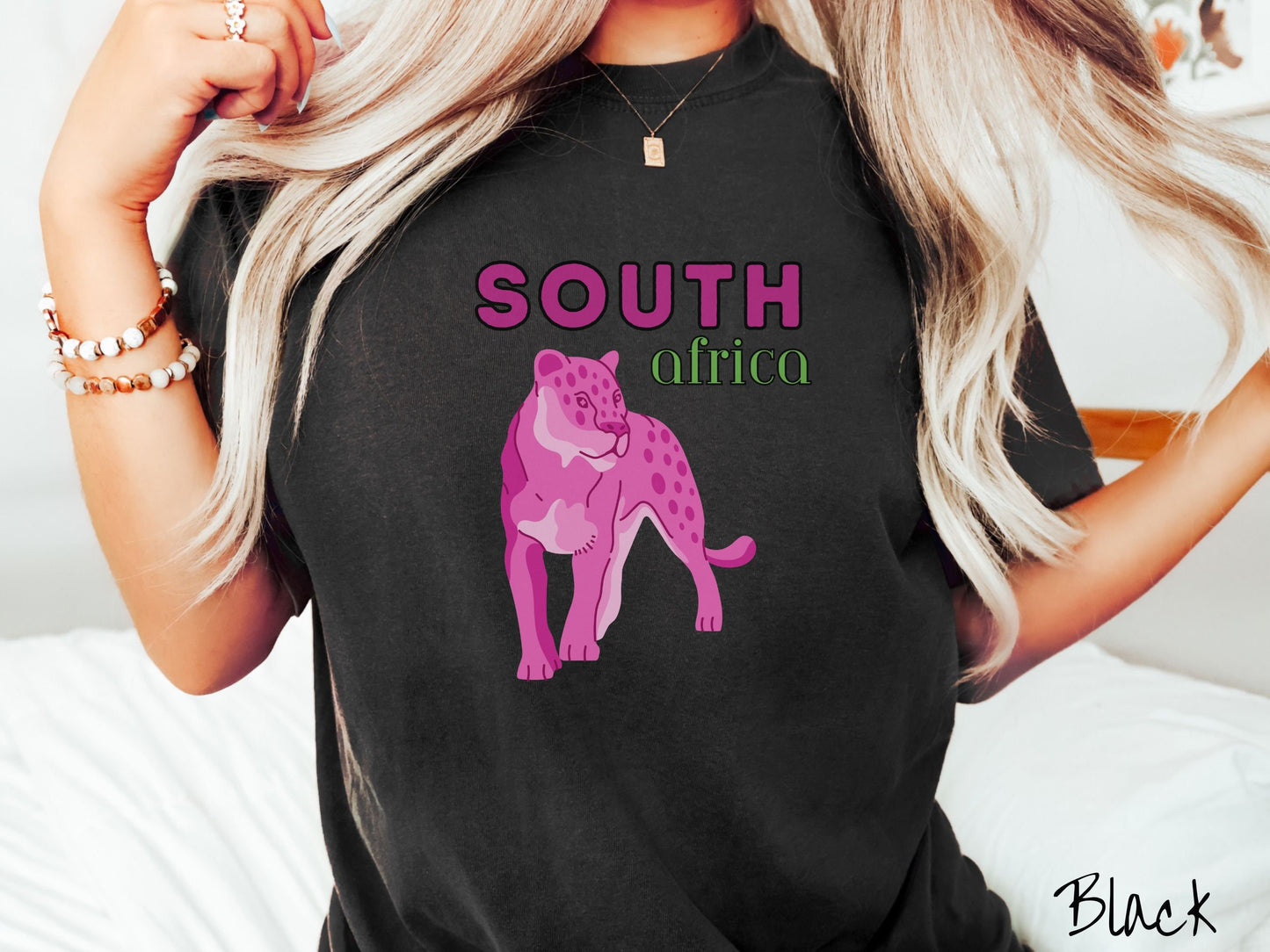 A woman wearing a vintage, black colored shirt with the text South Africa in pink and green font, respectively, and a pink tiger underneath on the prowl.