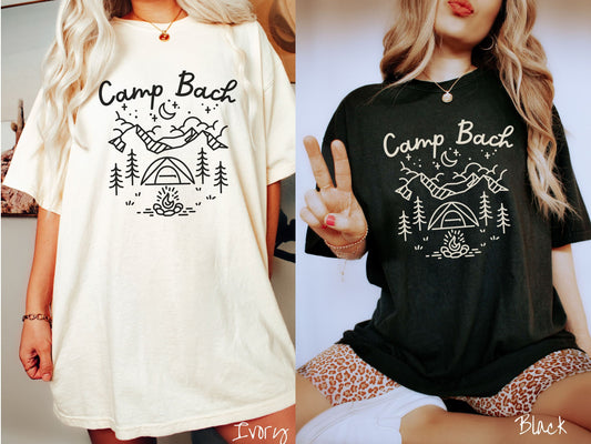 Two women wearing cute, vintage ivory and black colored Comfort Colors t-shirts with text Camp Bach in white, cursive font. Above the text are outlines of mountains, trees, stars, a tent, campfire, and a stream.