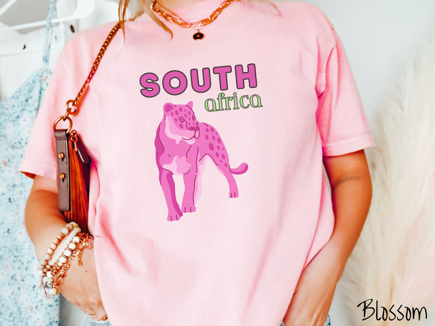 A woman wearing a vintage, blossom colored shirt with the text South Africa in pink and green font, respectively, and a pink tiger underneath on the prowl.
