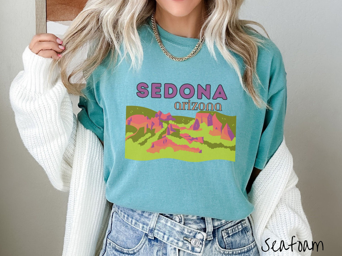 A woman wearing a vintage, seafoam colored shirt with the text Sedona Arizona in purple and orange font, respectively, and below that is a picture of red rock canyons and green meadows.