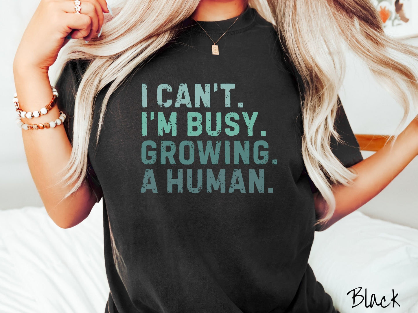 A woman wearing a vintage, black colored Comfort Colors t-shirt with the text listed vertically in varying shades of green font I Can’t. I’m busy. Growing. A human.