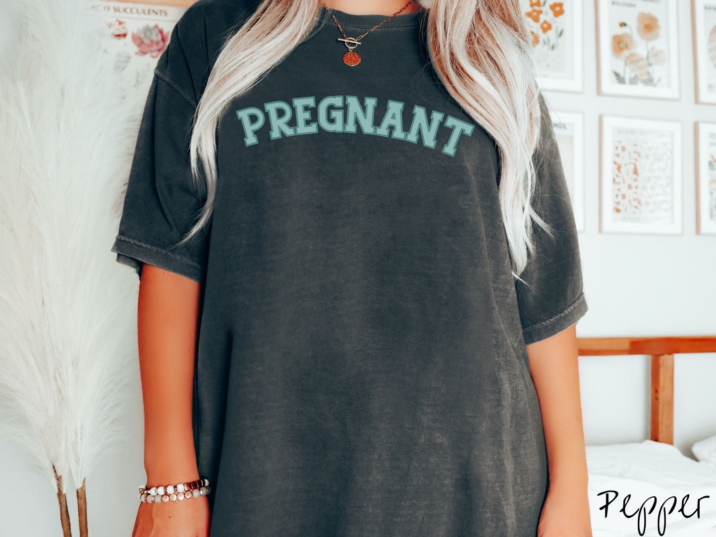 A woman wearing a vintage, pepper colored Comfort Colors t-shirt with the text PREGNANT in light green and dark green outlined uppercase font.