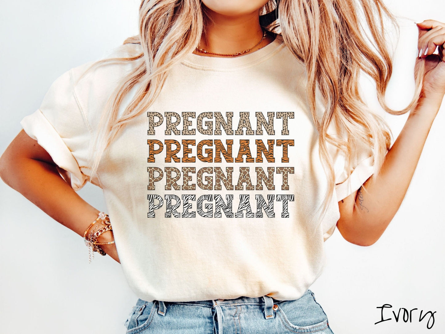 A woman wearing a vintage, ivory colored Comfort Colors t-shirt with the text PREGNANT in uppercase font listed four times vertically. One has leopard font, another tiger font, another zebra stripes, and the last is zebra stripe font.