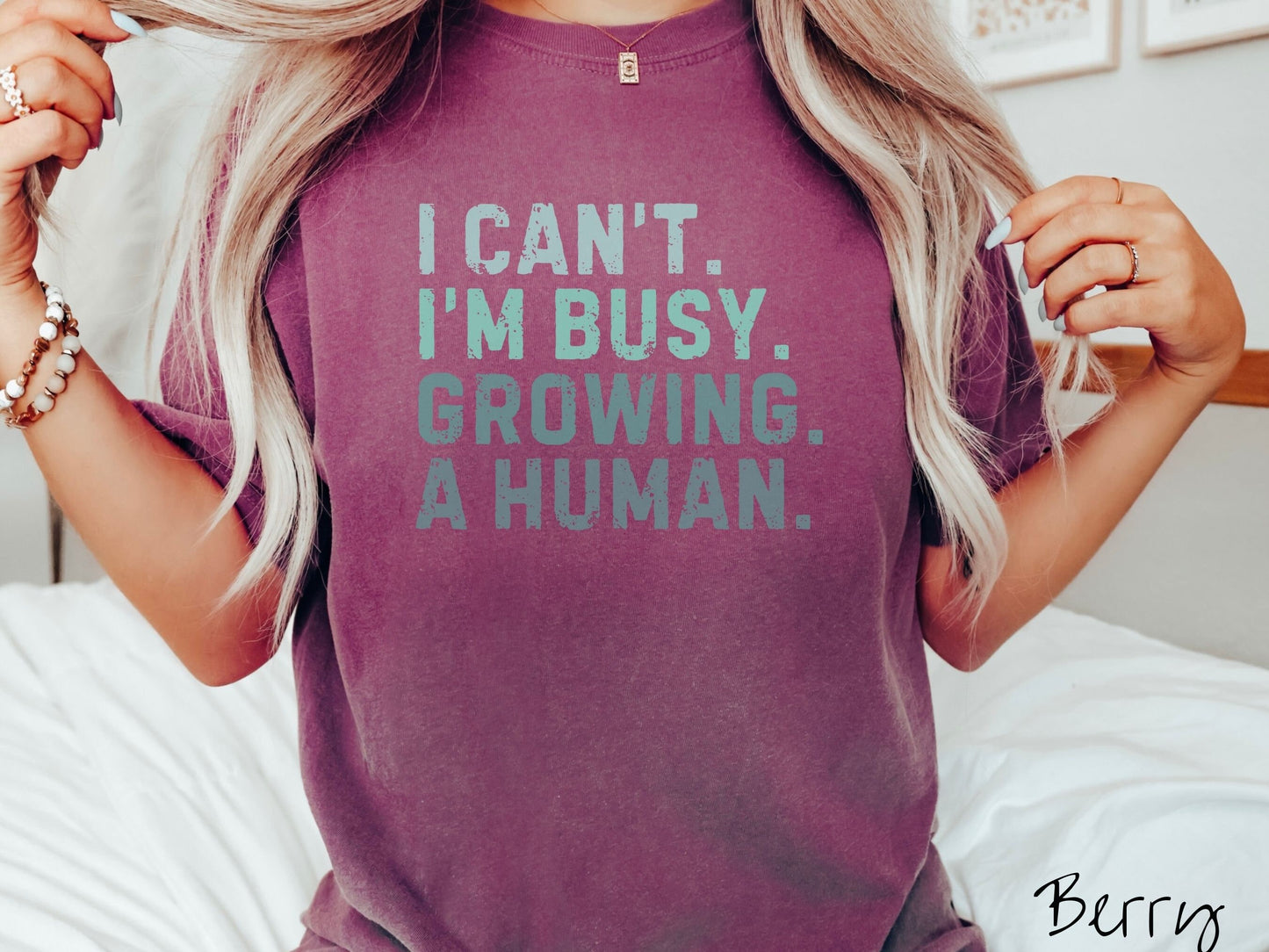 A woman wearing a vintage, berry colored Comfort Colors t-shirt with the text listed vertically in varying shades of green font I Can’t. I’m busy. Growing. A human.
