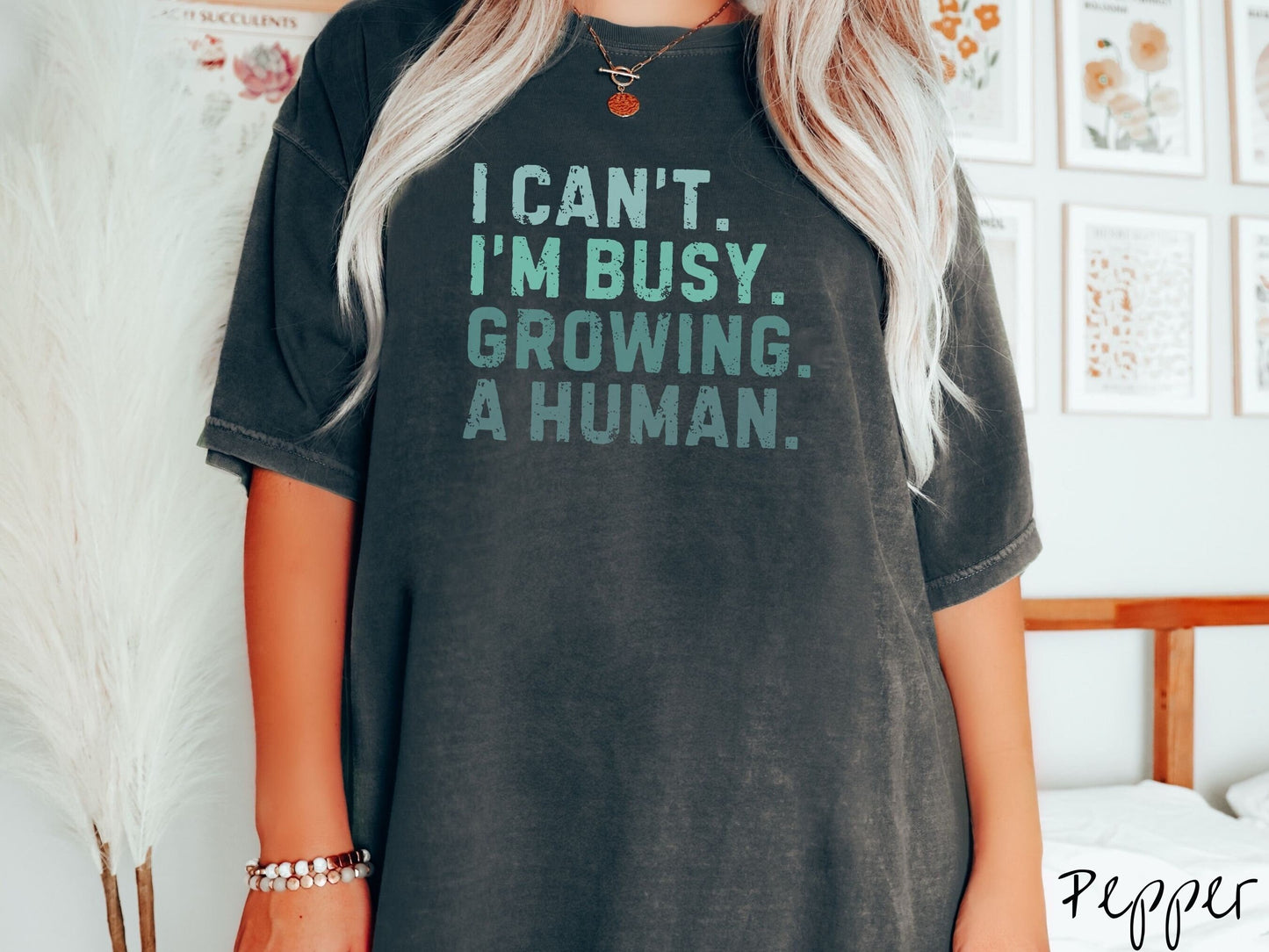 A woman wearing a vintage, pepper colored Comfort Colors t-shirt with the text listed vertically in varying shades of green font I Can’t. I’m busy. Growing. A human.