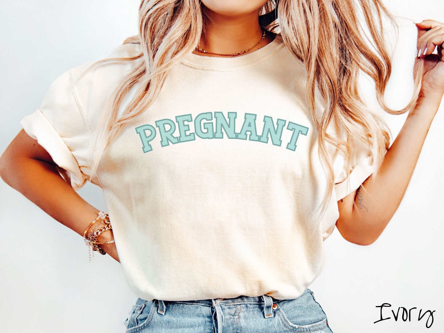 A woman wearing a vintage, ivory colored Comfort Colors t-shirt with the text PREGNANT in light green and dark green outlined uppercase font.