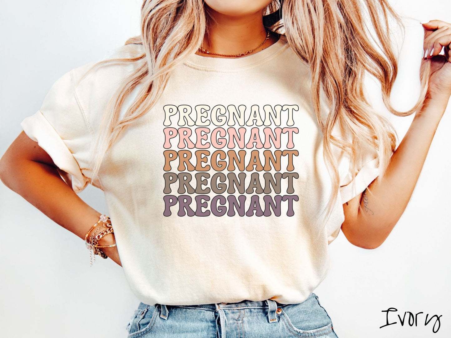 A woman wearing a vintage, ivory colored Comfort Colors t-shirt with the text PREGNANT in uppercase font listed five times vertically. One is ivory colored, the next pink, next light brown, next dark brown, and the fifth is purple.