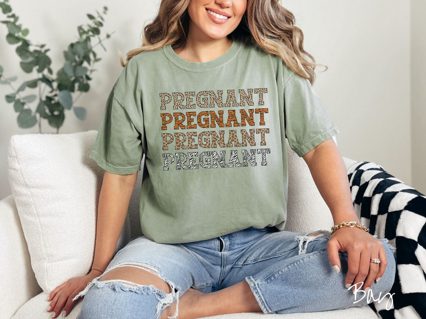 A woman wearing a vintage, bay colored Comfort Colors t-shirt with the text PREGNANT in uppercase font listed four times vertically. One has leopard font, another tiger font, another zebra stripes, and the last is zebra stripe font.