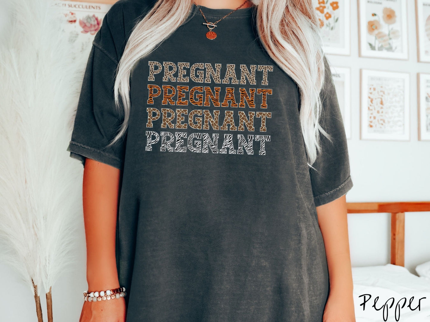 A woman wearing a vintage, pepper colored Comfort Colors t-shirt with the text PREGNANT in uppercase font listed four times vertically. One has leopard font, another tiger font, another zebra stripes, and the last is zebra stripe font.