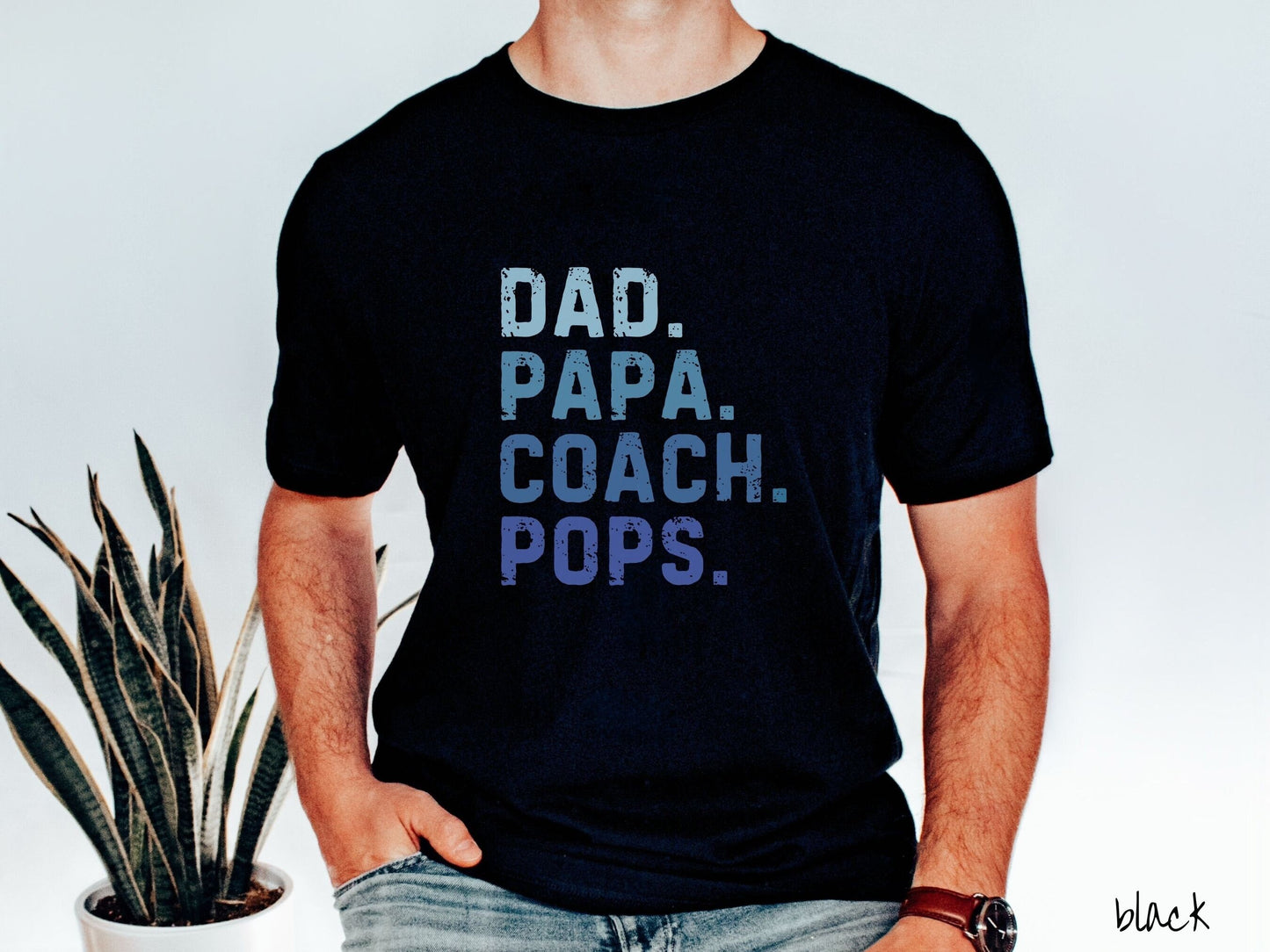 A man wearing a vintage, black colored Comfort Colors t-shirt with the text in varying blue colored font Dad. Papa. Coach. Pops.