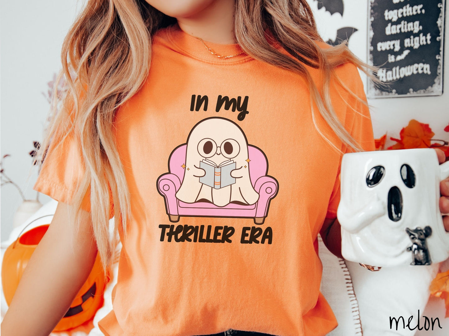 A woman wearing a vintage, melon colored Comfort Colors t-shirt with the text In My Thriller Era across the front in black font. In between the text is a young ghost with glasses reading a book and sitting in a pink chair.