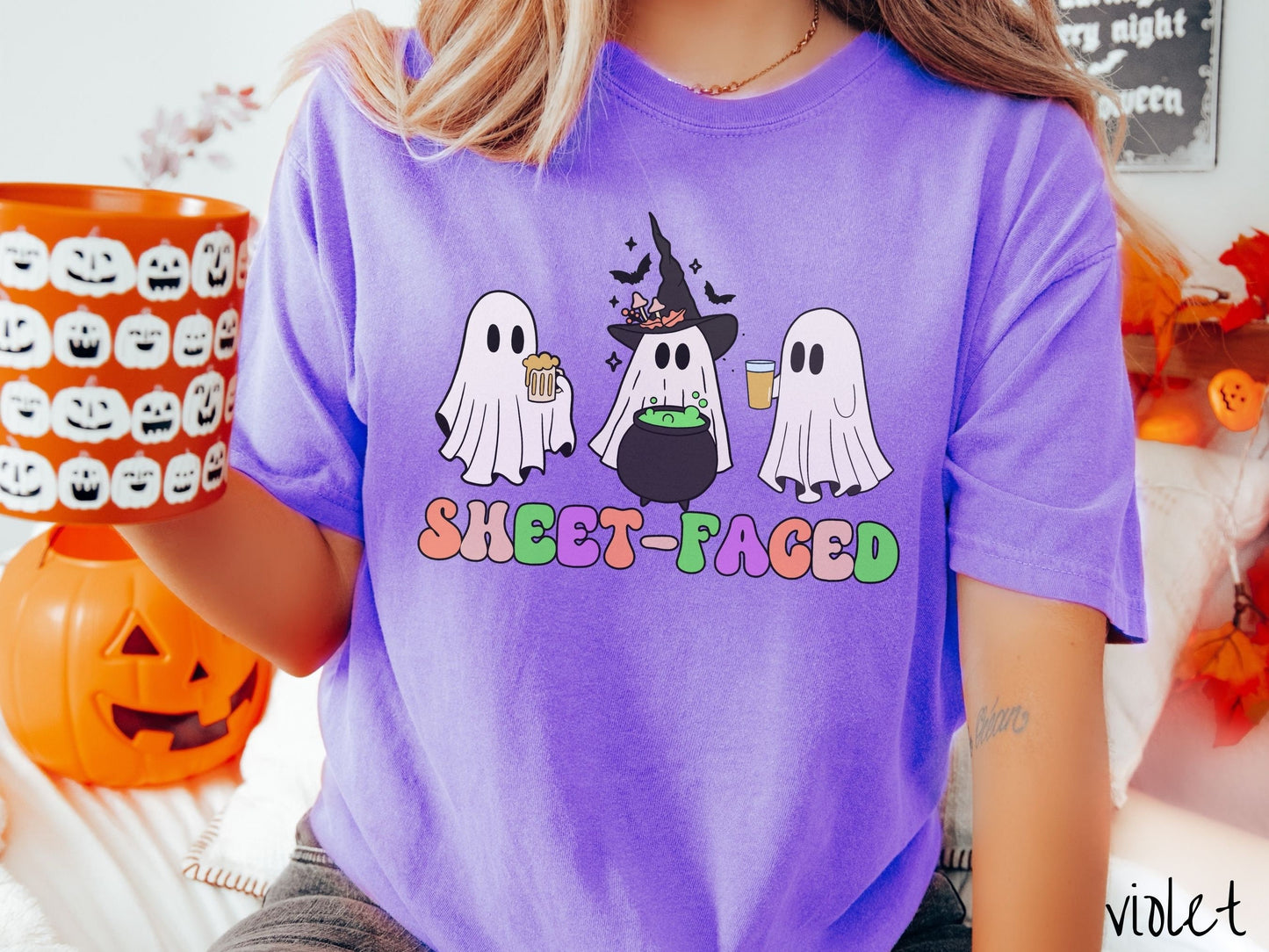 A woman wearing a vintage, violet colored Comfort Colors t-shirt with the text Sheet-Faced in colorful font across the front. Above are three white ghosts drinking beers and standing around a black cauldron with a bubbling green liquid in it.