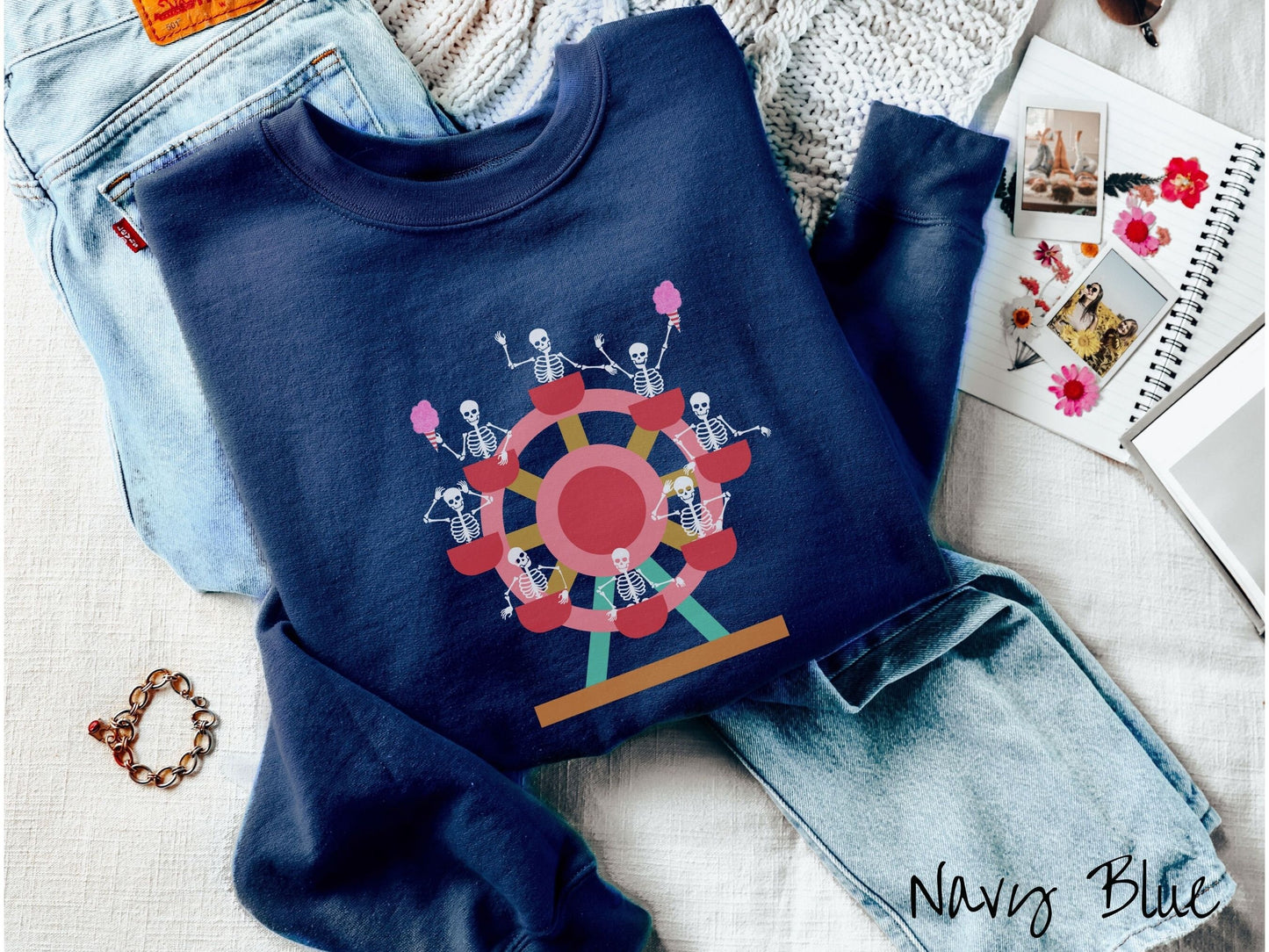 A cute navy blue colored comfy sweatshirt with a ferris wheel filled with black skeletons waving and holding cotton candy as they go around the ride.