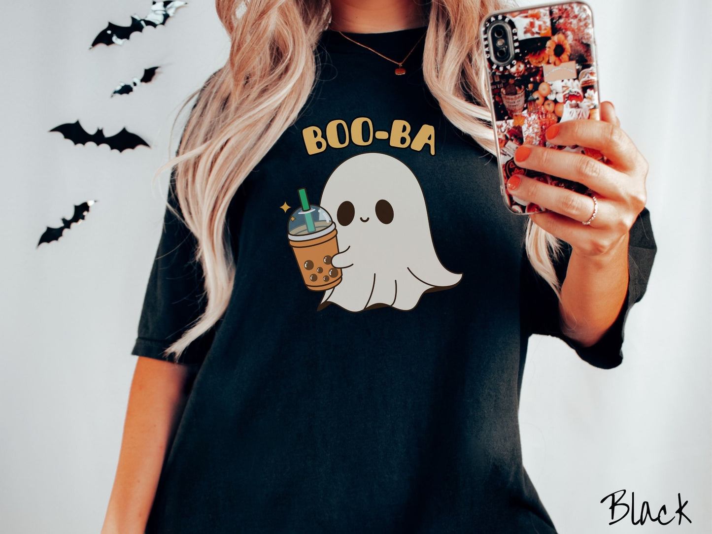 A woman wearing a cute, vintage black colored Comfort Colors T-shirt with the text Boo-Ba in yellow font across the top. Below is a little smiling white sheet ghost holding a light brown boba tea in a plastic to-go cup.
