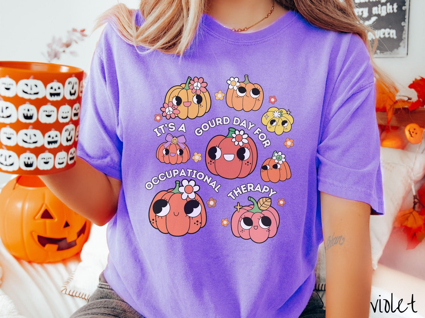 A woman wearing a cute, vintage violet colored Comfort Colors T-shirt with text Its a Gourd Day for Occupational Therapy in white font. There is a three by three grid of orange, yellow, and pink pumpkins with girly eyes, wearing flowers and bows.