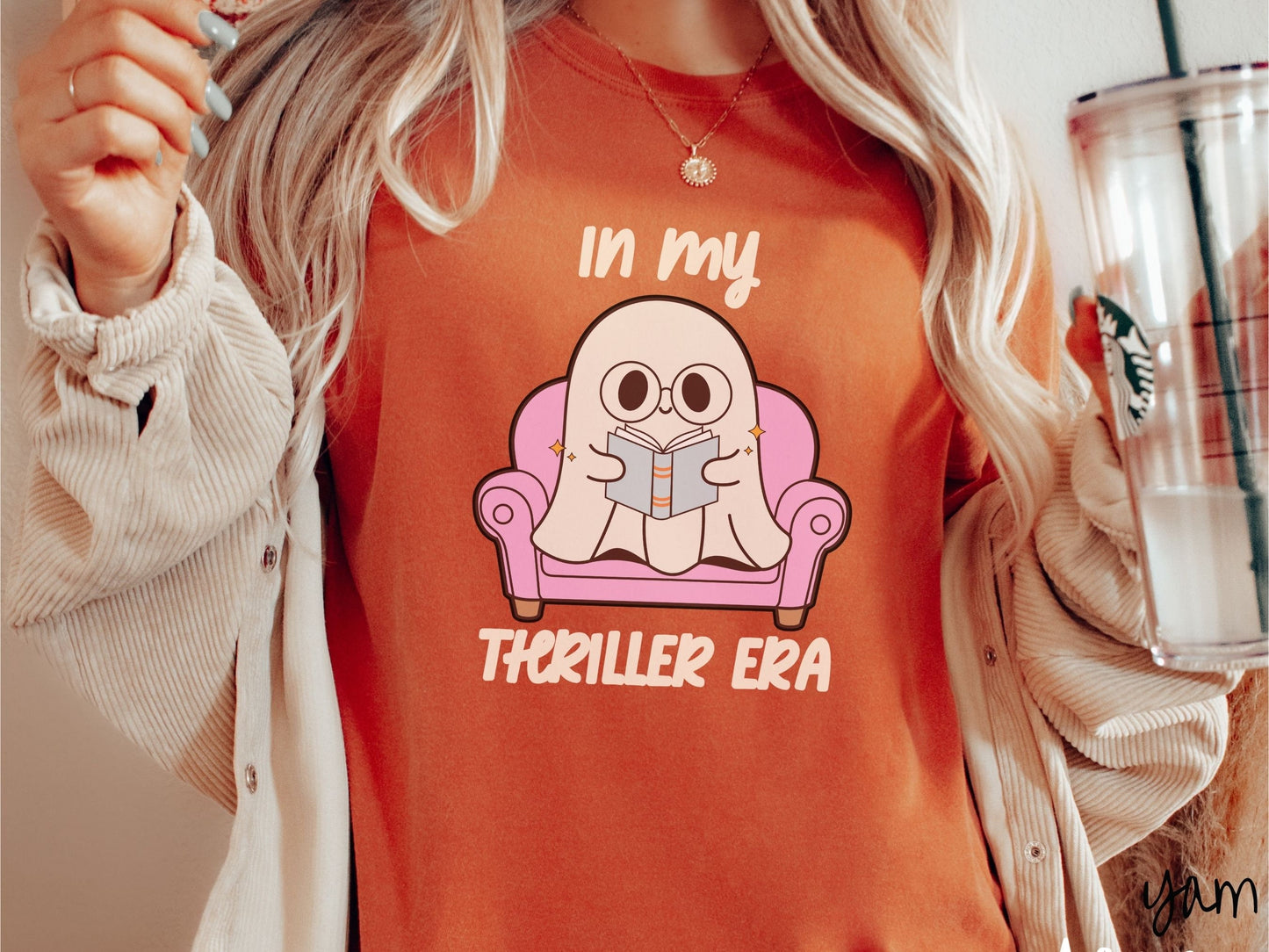 A woman wearing a vintage, yam colored Comfort Colors t-shirt with the text In My Thriller Era across the front in ivory font. In between the text is a young ghost with glasses reading a book and sitting in a pink chair.
