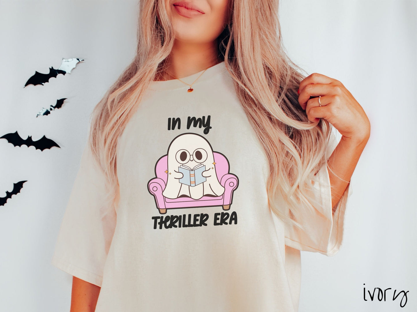 A woman wearing a vintage, ivory colored Comfort Colors t-shirt with the text In My Thriller Era across the front in black font. In between the text is a young ghost with glasses reading a book and sitting in a pink chair.