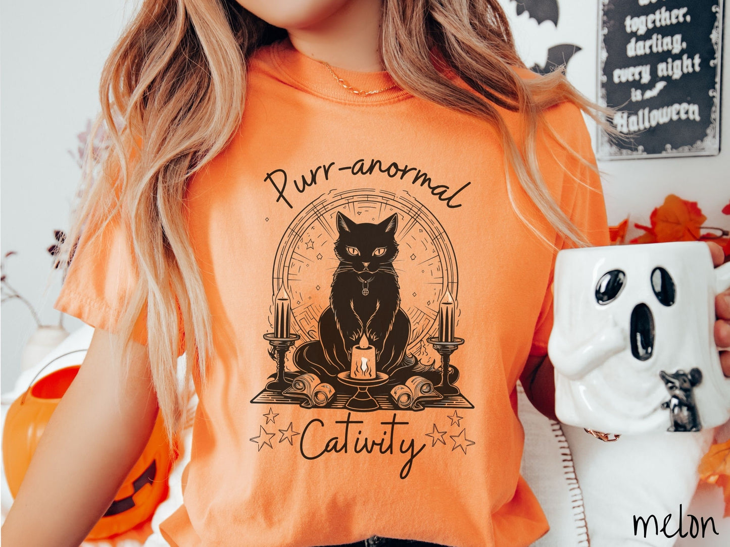 A woman wearing a cute, vintage melon colored Comfort Colors T-shirt with text Purr-anormal Cativity in black font. There is a black cat sitting on an altar with candles and scrolls, staring straight forward with piercing eyes and wearing a necklace.