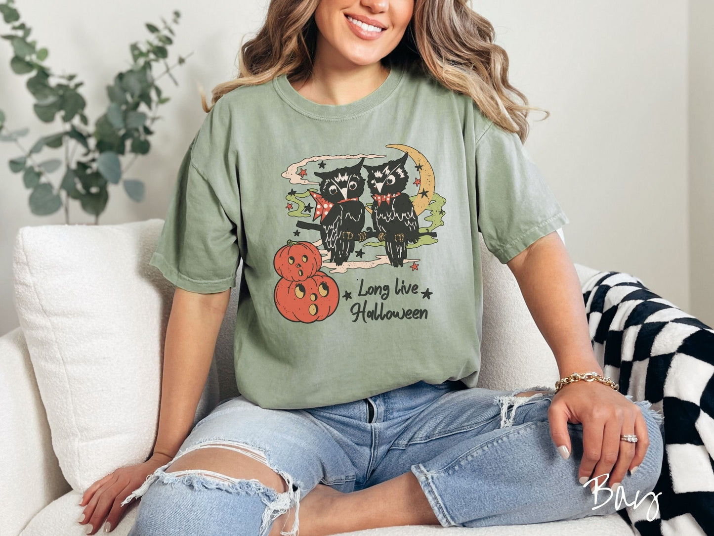 A woman wearing a cute, vintage bay colored Comfort Colors T-shirt with the text Long Live Halloween in black font. Above are two black owls sitting on a tree branch by two scared pumpkins and surrounded by stars and the moon.