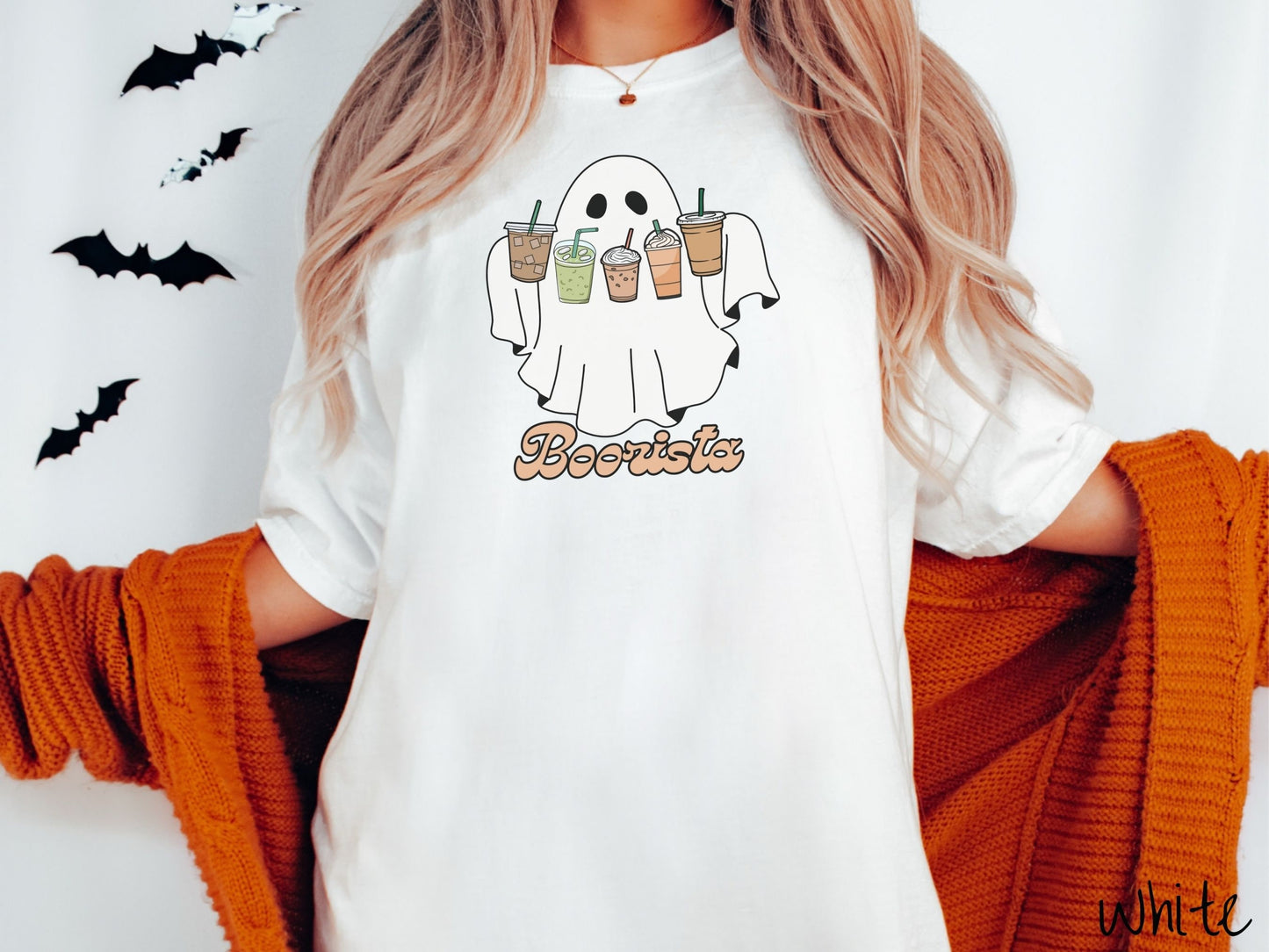 A woman wearing a cute, vintage white colored Comfort Colors T-shirt with the text Boorista along the bottom. Above is a white ghost holding an iced coffee, a green matcha tea, a frappuccino, a pumpkin spiced latte, and an iced mocha latte.