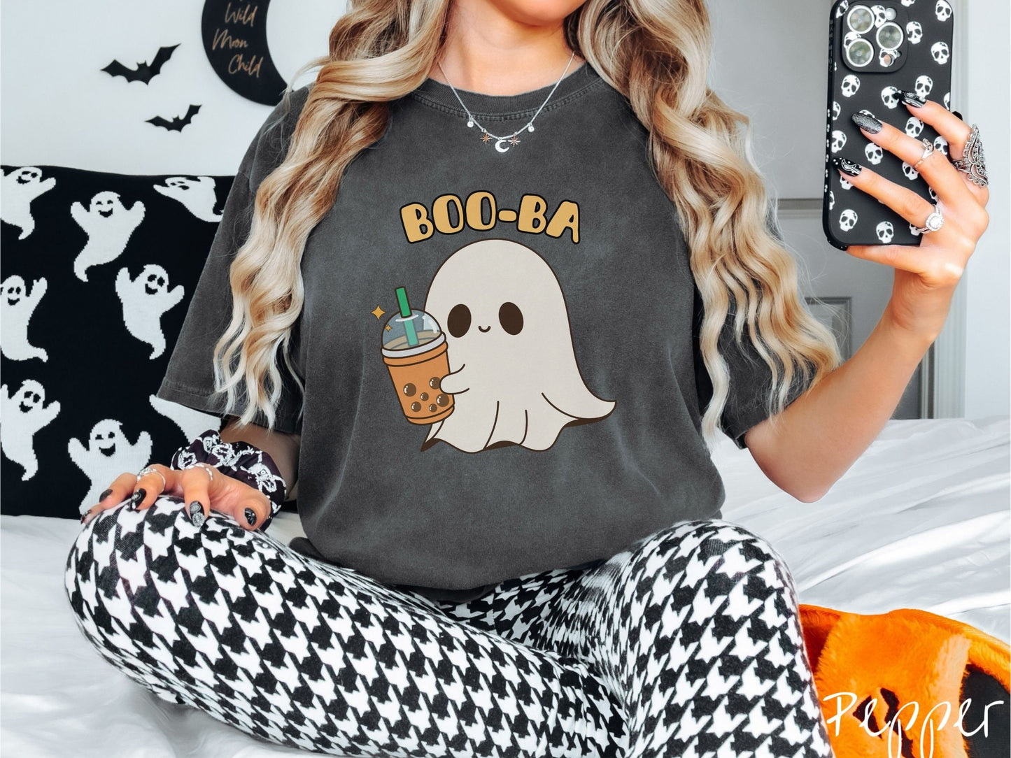 A woman wearing a cute, vintage pepper colored Comfort Colors T-shirt with the text Boo-Ba in yellow font across the top. Below is a little smiling white sheet ghost holding a light brown boba tea in a plastic to-go cup.