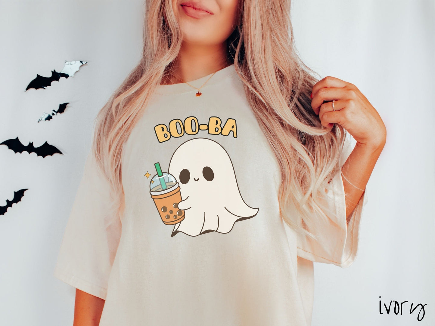A woman wearing a cute, vintage ivory colored Comfort Colors T-shirt with the text Boo-Ba in yellow font across the top. Below is a little smiling white sheet ghost holding a light brown boba tea in a plastic to-go cup.