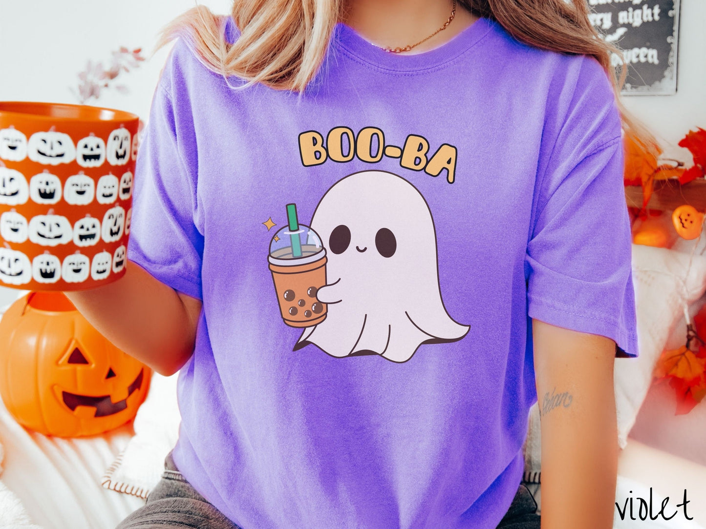 A woman wearing a cute, vintage violet colored Comfort Colors T-shirt with the text Boo-Ba in yellow font across the top. Below is a little smiling white sheet ghost holding a light brown boba tea in a plastic to-go cup.