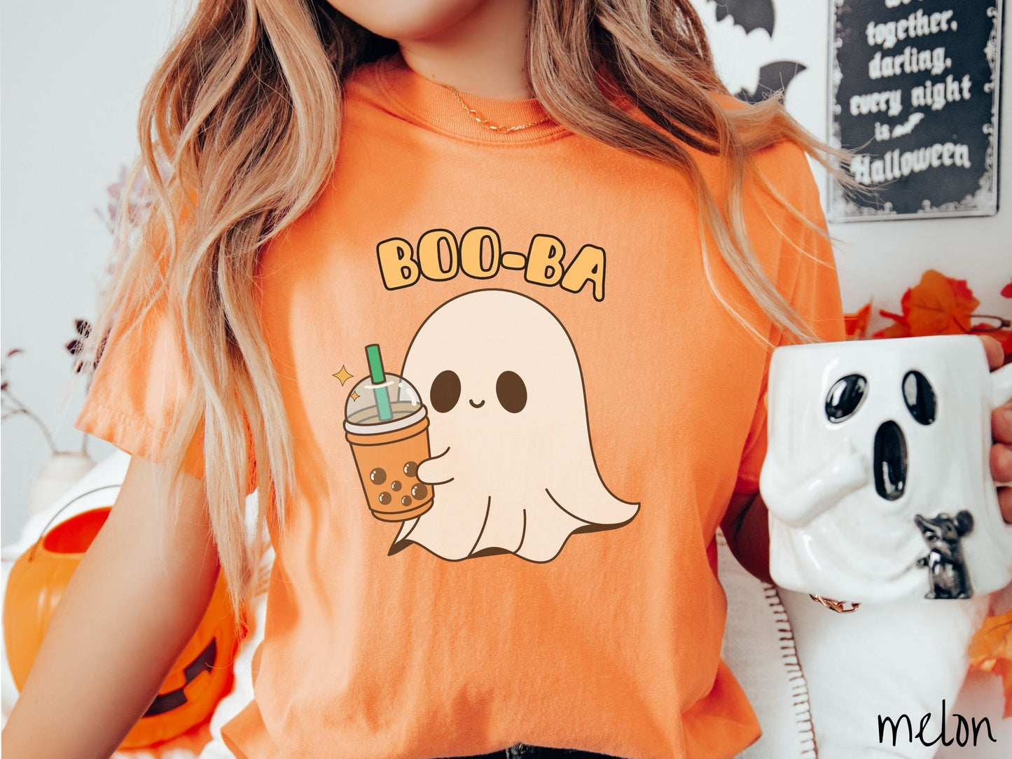 A woman wearing a cute, vintage melon colored Comfort Colors T-shirt with the text Boo-Ba in yellow font across the top. Below is a little smiling white sheet ghost holding a light brown boba tea in a plastic to-go cup.