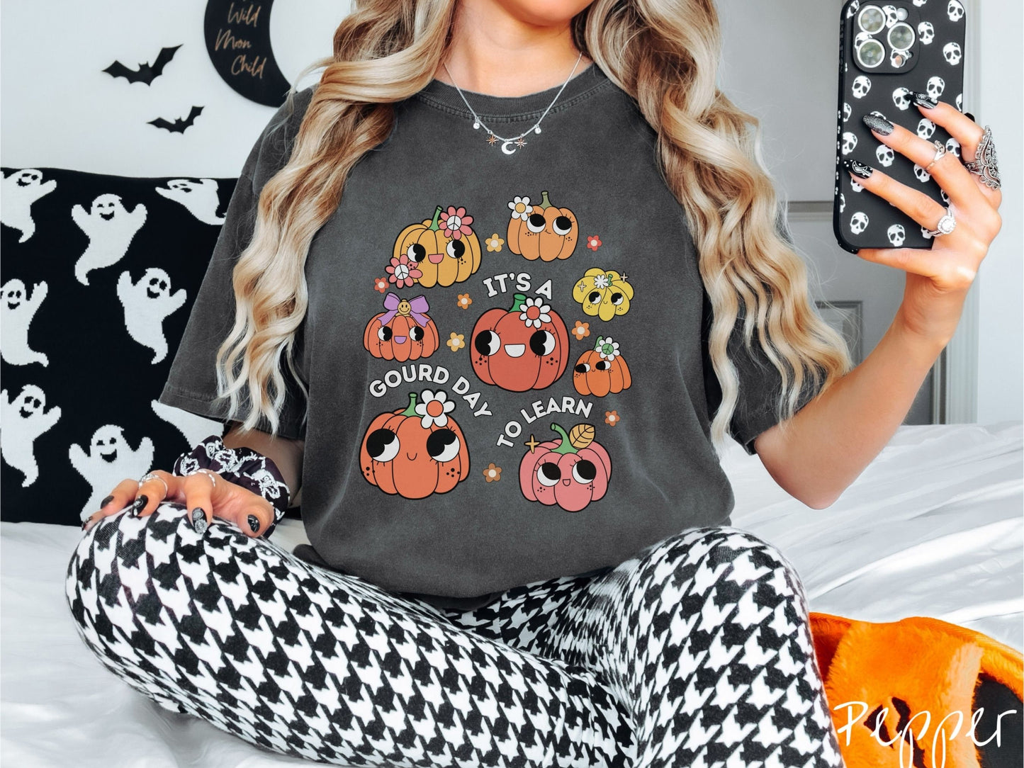 A woman wearing a cute, vintage pepper colored Comfort Colors T-shirt with the text Its a Gourd Day to Learn in white font. There is a three by three grid of orange, yellow, and pink pumpkins with girly eyes, wearing flowers and bows.