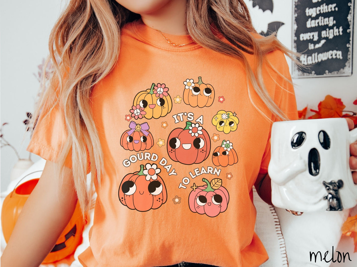 A woman wearing a cute, vintage melon colored Comfort Colors T-shirt with the text Its a Gourd Day to Learn in white font. There is a three by three grid of orange, yellow, and pink pumpkins with girly eyes, wearing flowers and bows.