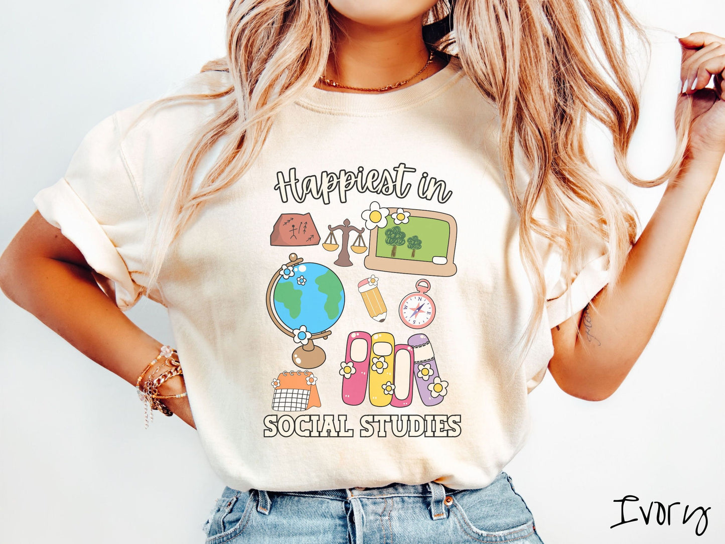 A woman wearing a cute, vintage ivory colored Comfort Colors T-shirt with the text Happiest in Social Studies Class. In between the text are hieroglyphics, a globe, a pencil, compass, books, laptop computer, and a weight scale.