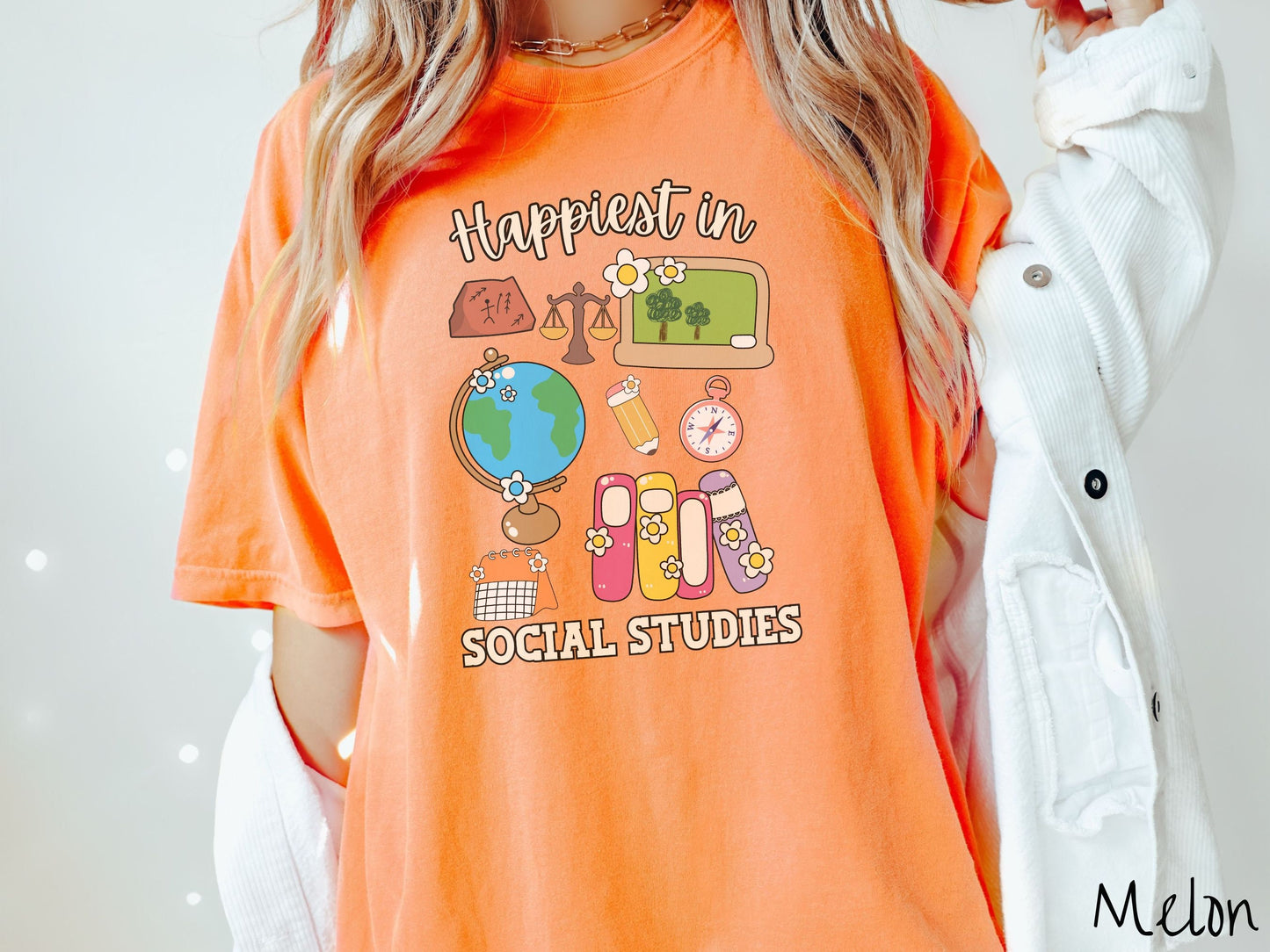 A woman wearing a cute, vintage melon colored Comfort Colors T-shirt with the text Happiest in Social Studies Class. In between the text are hieroglyphics, a globe, a pencil, compass, books, laptop computer, and a weight scale.