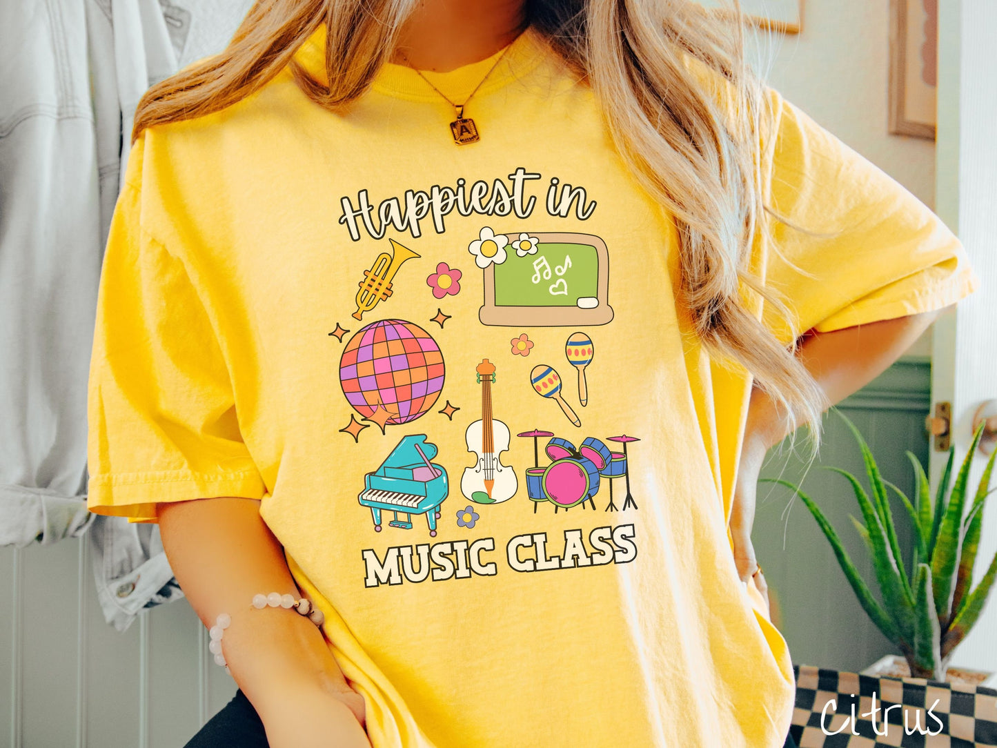 A woman wearing a cute, vintage citrus colored Comfort Colors T-shirt with the text Happiest in Music Class. In between the text are a saxophone, a disco ball, a chalkboard, a piano, a guitar, a drum set, maracas, and flowers.