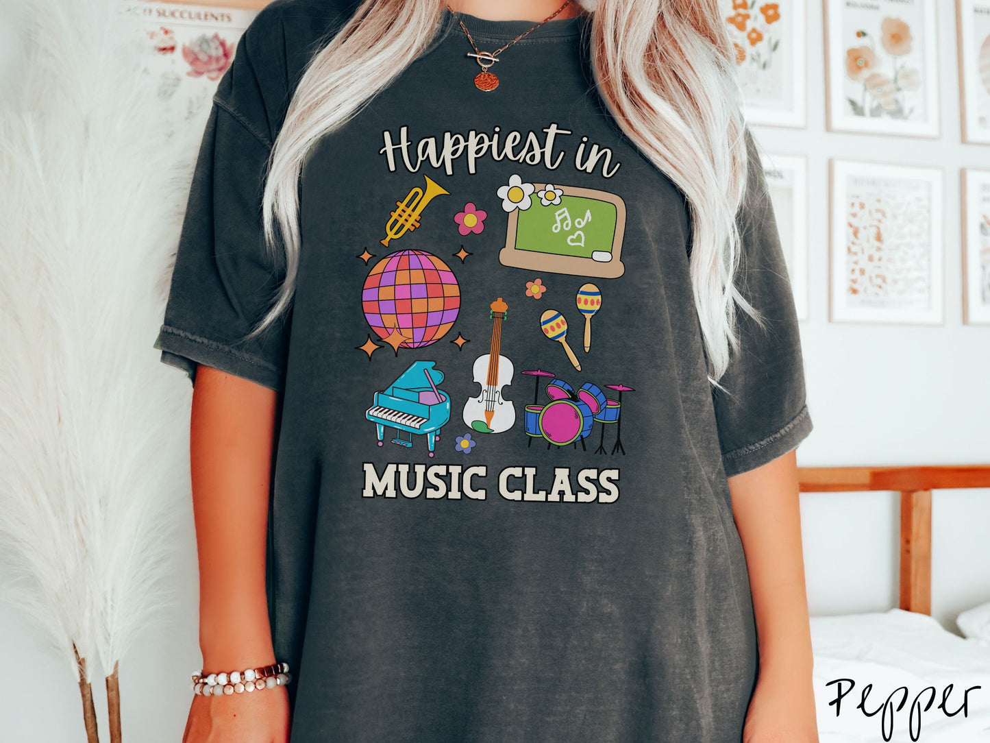 A woman wearing a cute, vintage pepper colored Comfort Colors T-shirt with the text Happiest in Music Class. In between the text are a saxophone, a disco ball, a chalkboard, a piano, a guitar, a drum set, maracas, and flowers.