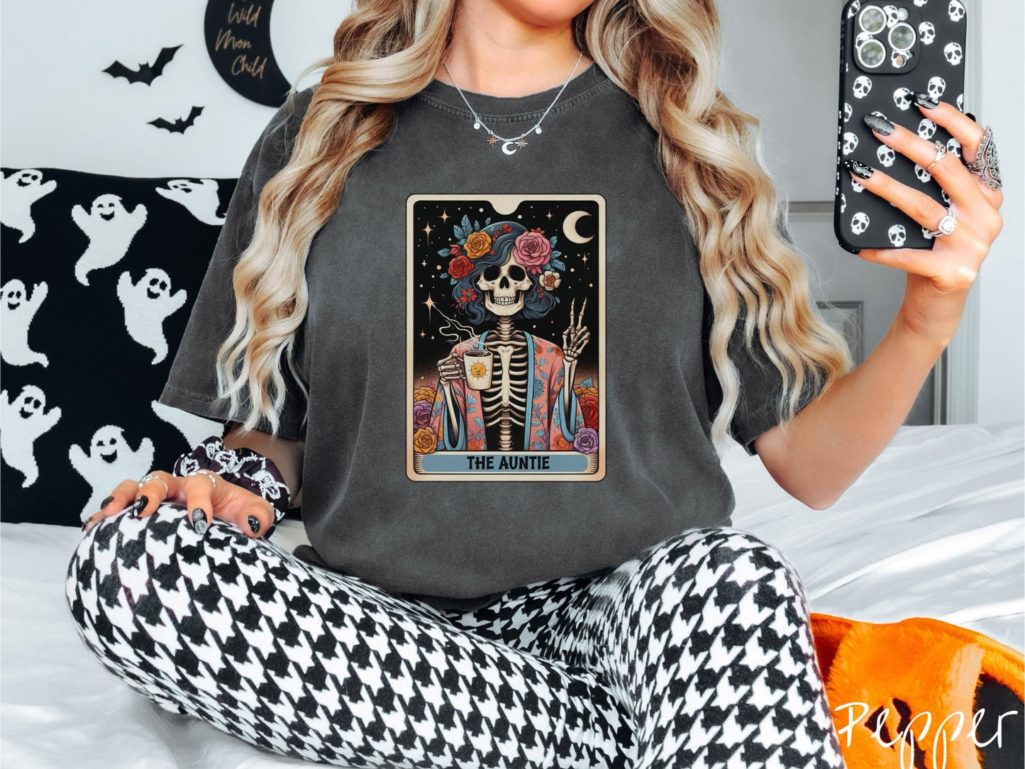 A woman wearing a cute, vintage pepper colored Comfort Colors T-shirt with text The Auntie along the bottom of a tarot card. Above is a picture of a female skeleton holding up a peace sign and wearing a flower robe holding a steaming cup of coffee.