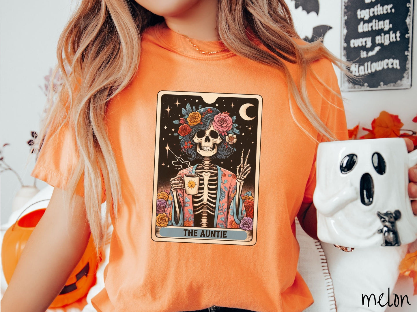 A woman wearing a cute, vintage melon colored Comfort Colors T-shirt with text The Auntie along the bottom of a tarot card. Above is a picture of a female skeleton holding up a peace sign and wearing a flower robe holding a steaming cup of coffee.