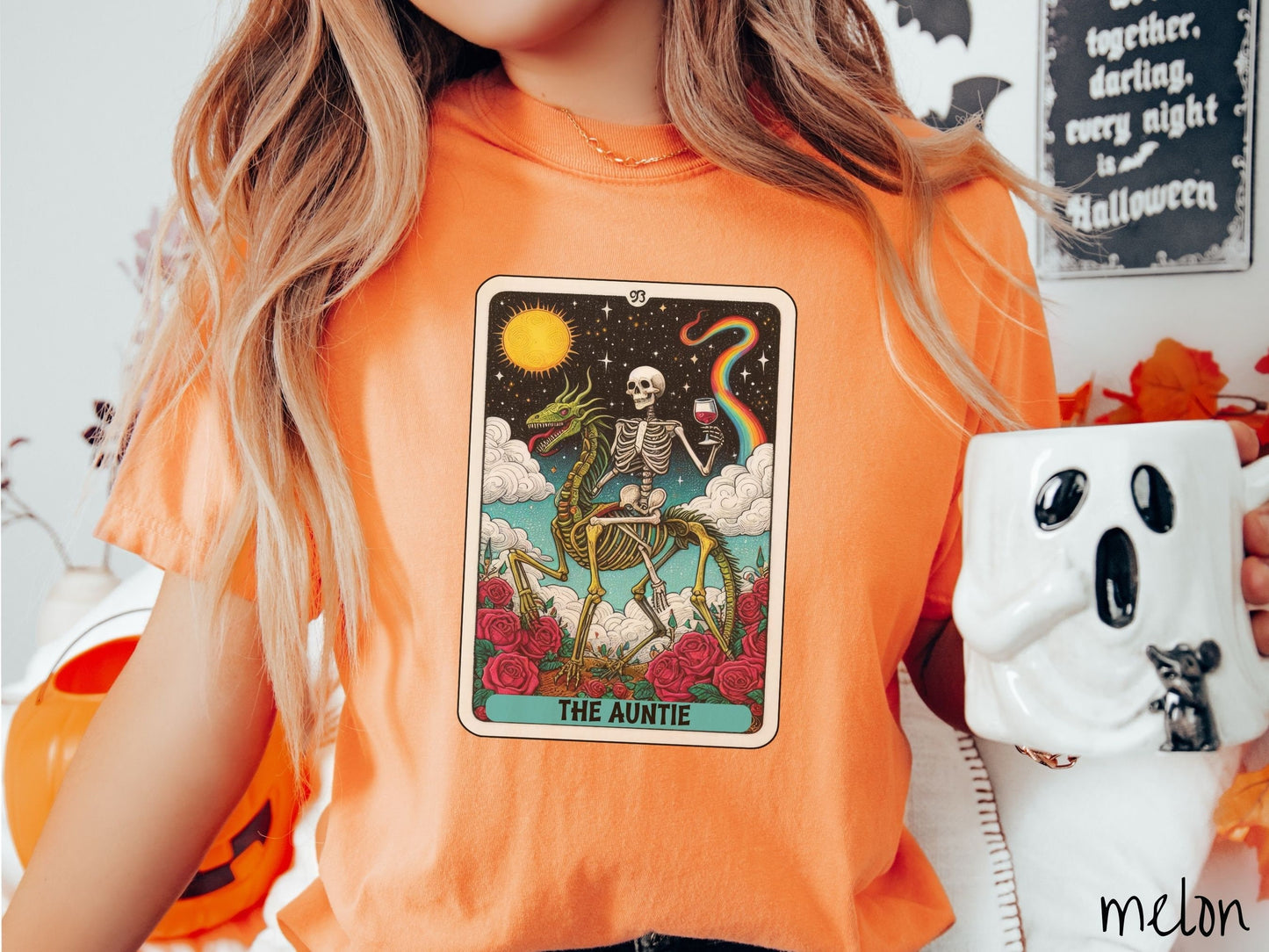 A woman wearing a cute, vintage melon colored Comfort Colors T-shirt with text The Auntie along the bottom of a tarot card. Above is a skeleton riding a skeleton horse and holding a glass of wine above roses with clouds and stars in the background.
