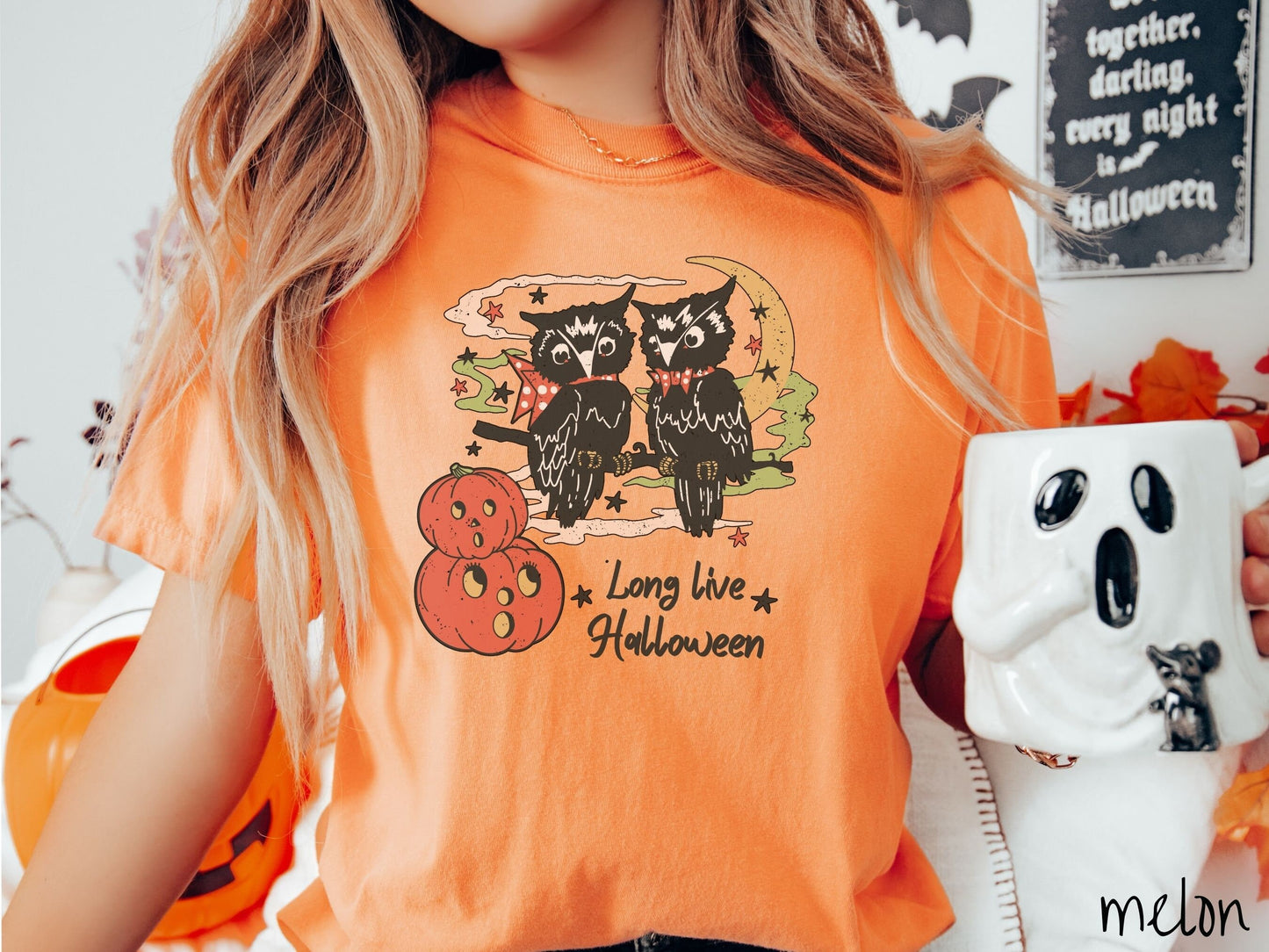 A woman wearing a cute, vintage melon colored Comfort Colors T-shirt with the text Long Live Halloween in black font. Above are two black owls sitting on a tree branch by two scared pumpkins and surrounded by stars and the moon.
