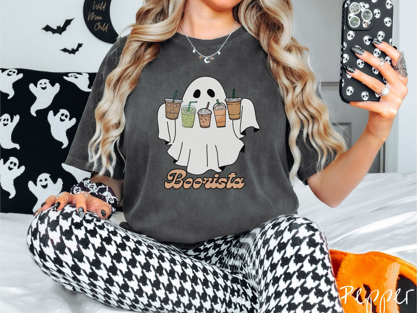 A woman wearing a cute, vintage pepper colored Comfort Colors T-shirt with the text Boorista along the bottom. Above is a white ghost holding an iced coffee, a green matcha tea, a frappuccino, a pumpkin spiced latte, and an iced mocha latte.