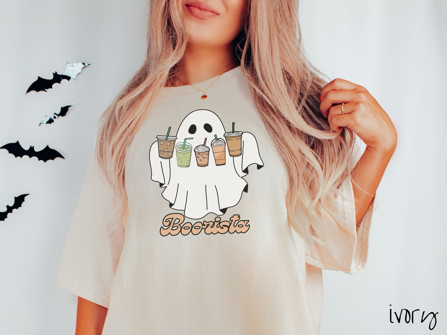 A woman wearing a cute, vintage ivory colored Comfort Colors T-shirt with the text Boorista along the bottom. Above is a white ghost holding an iced coffee, a green matcha tea, a frappuccino, a pumpkin spiced latte, and an iced mocha latte.