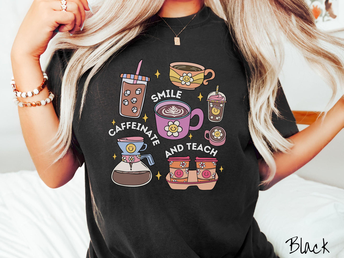 A woman wearing a cute, vintage black colored Comfort Colors T-shirt with text Smile Caffeinate and Teach. There is an iced coffee, two cups of hot coffee, a blended coffee drink with whipped cream, to-go coffees, and a pot of coffee.