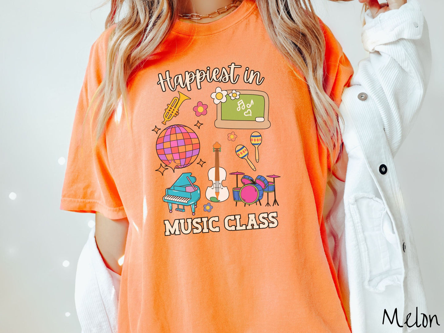 A woman wearing a cute, vintage melon colored Comfort Colors T-shirt with the text Happiest in Music Class. In between the text are a saxophone, a disco ball, a chalkboard, a piano, a guitar, a drum set, maracas, and flowers.