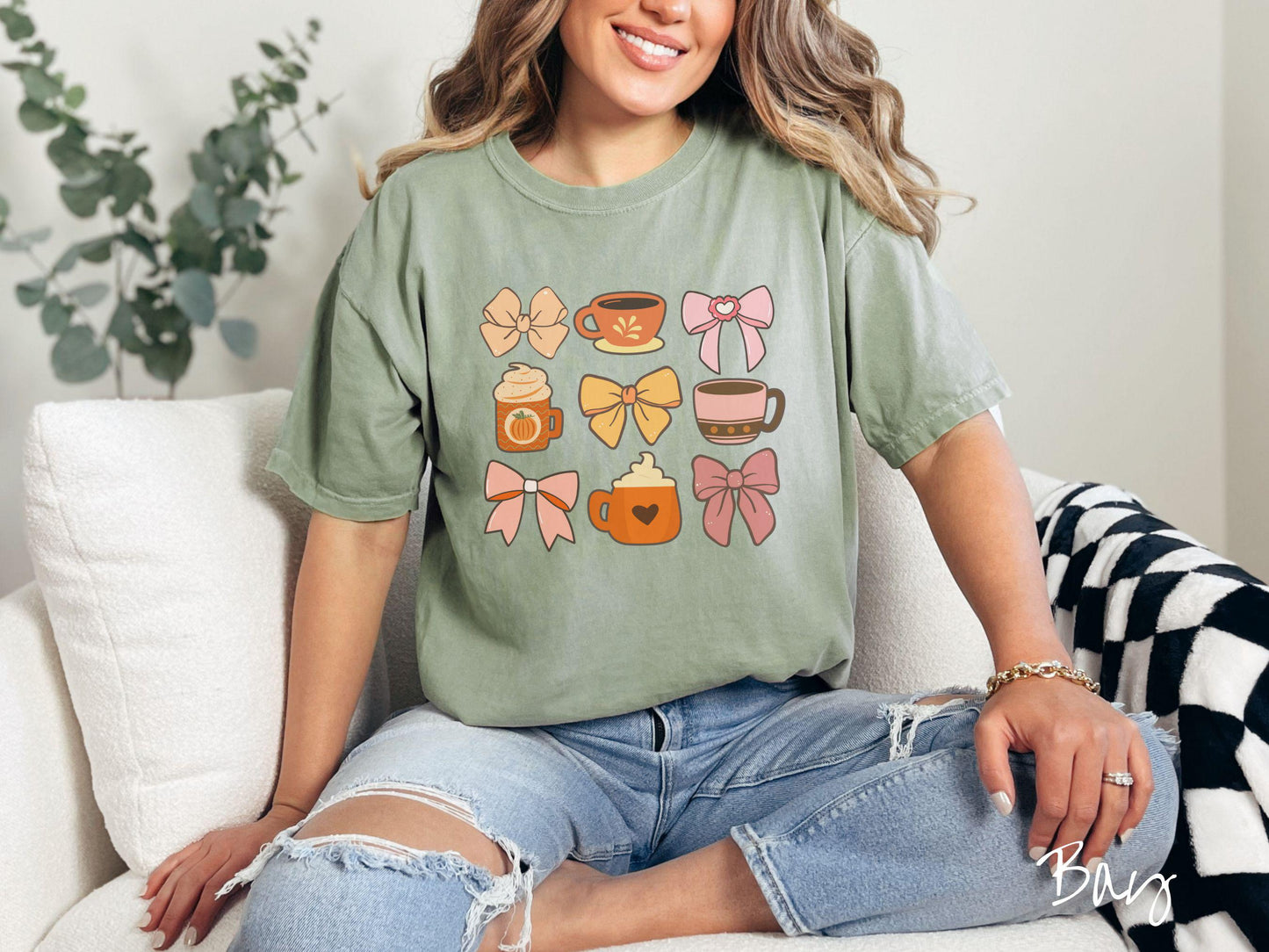 A woman wearing a cute, vintage bay colored Comfort Colors T-shirt with a grid of pictures of an orange bow, an orange tea cup, a pink bow, an orange pumpkin-spiced latte, a yellow bow, a pink coffee cup, a pink bow, and an orange coffee drink.