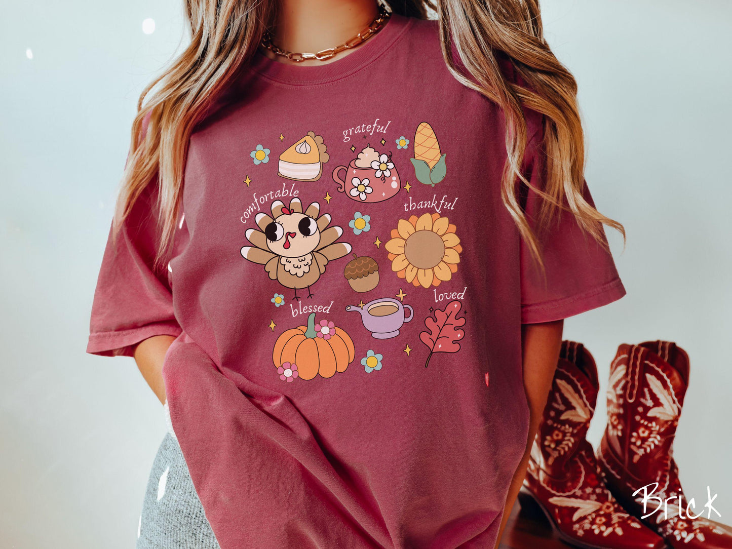 A woman wearing a cute, vintage brick colored Comfort Colors T-shirt with text grateful comfortable thankful blessed and love. In a grid format are a piece of pumpkin pie, a coffee mug, corn, a turkey, a sunflower, a pumpkin, a leaf, and an acorn.