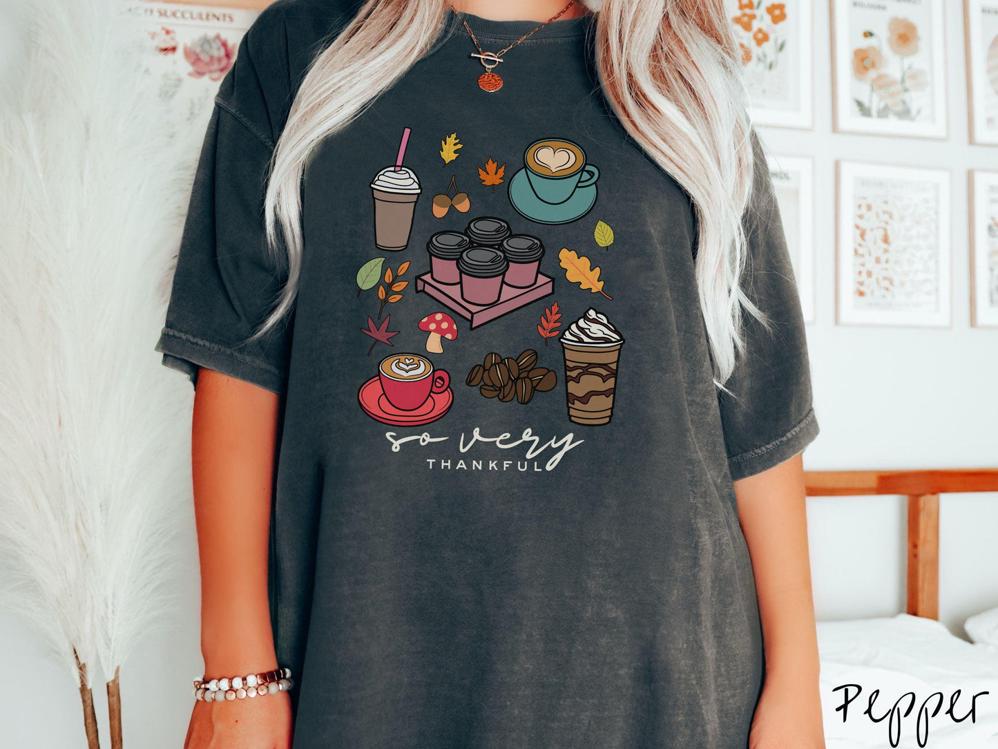 A woman wearing a cute, vintage pepper colored Comfort Colors T-shirt with the text so very thankful. Above are an iced coffee, four to-go cup coffees, a latte, a frappucino, coffee beans, mushrooms, and fall leaves scattered around.