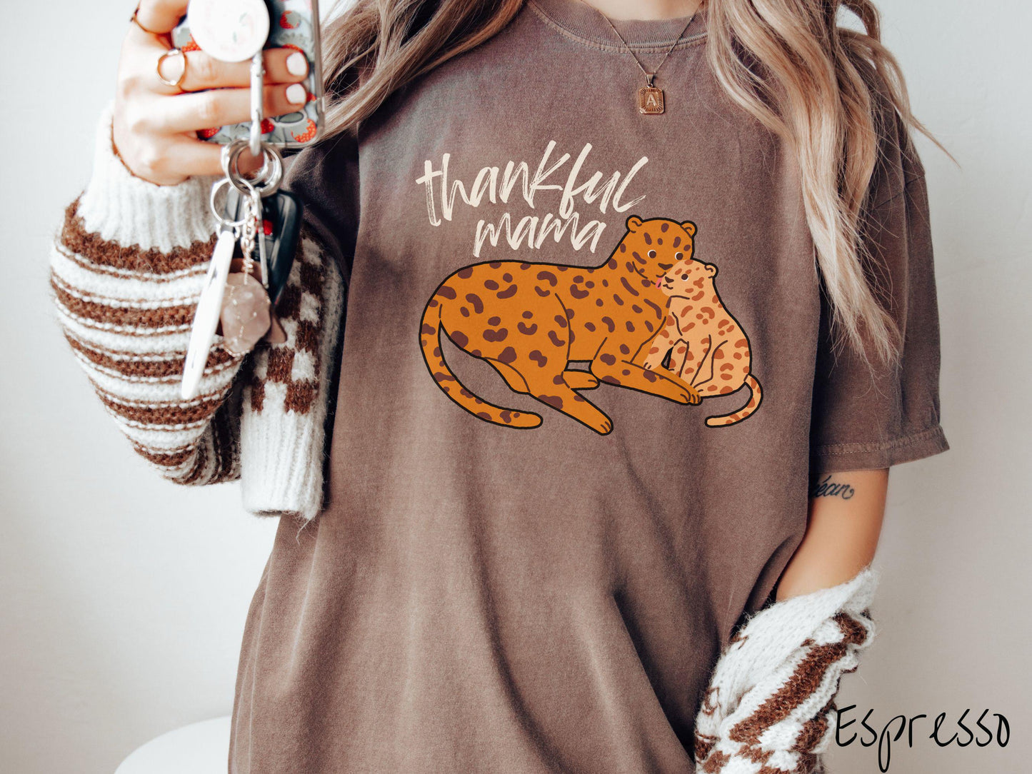 A woman wearing a cute, vintage espresso colored Comfort Colors T-shirt with the text thankful mama in black, sharpie font. Below is an orange, mother leopard coddling its child.