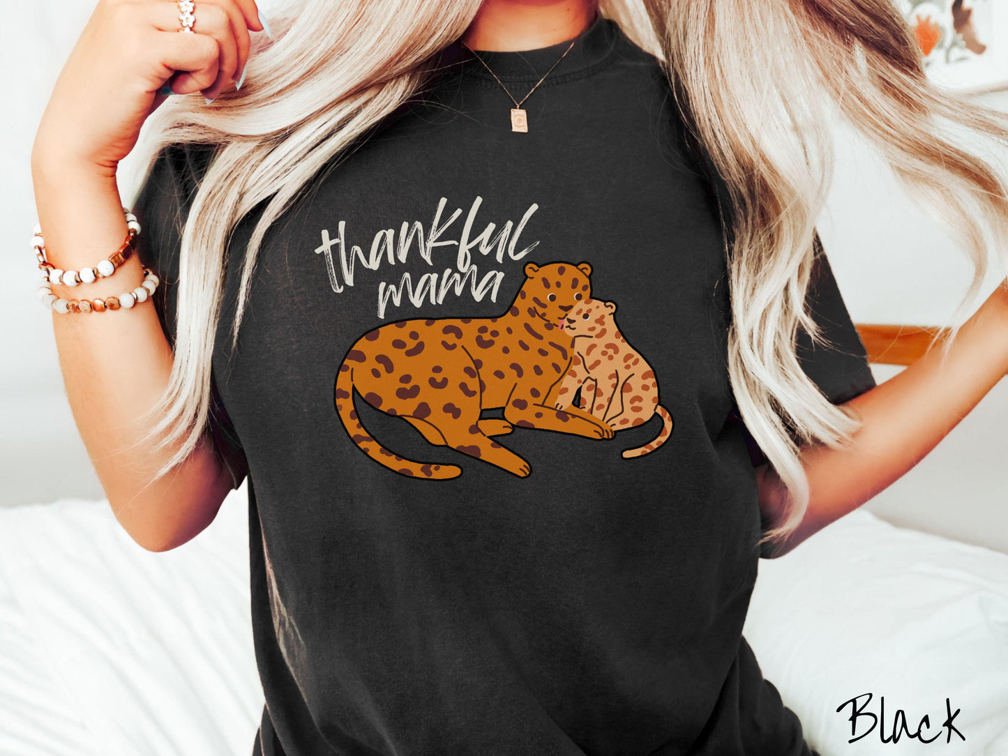 A woman wearing a cute, vintage black colored Comfort Colors T-shirt with the text thankful mama in black, sharpie font. Below is an orange, mother leopard coddling its child.