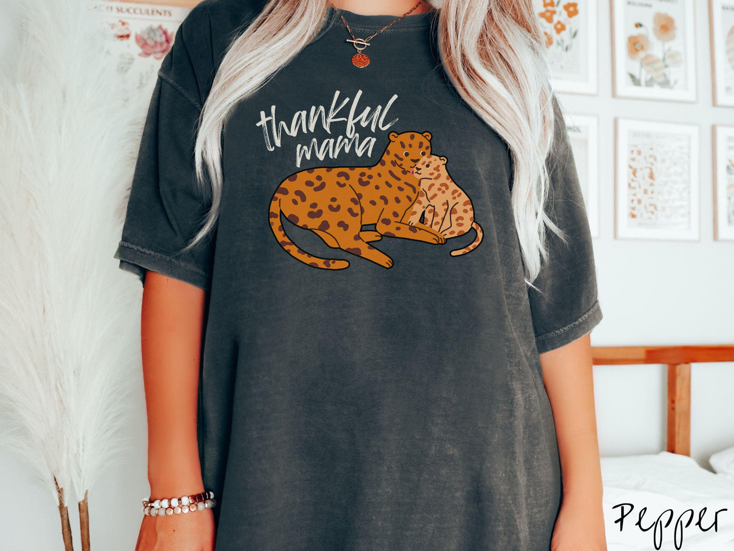 A woman wearing a cute, vintage pepper colored Comfort Colors T-shirt with the text thankful mama in black, sharpie font. Below is an orange, mother leopard coddling its child.
