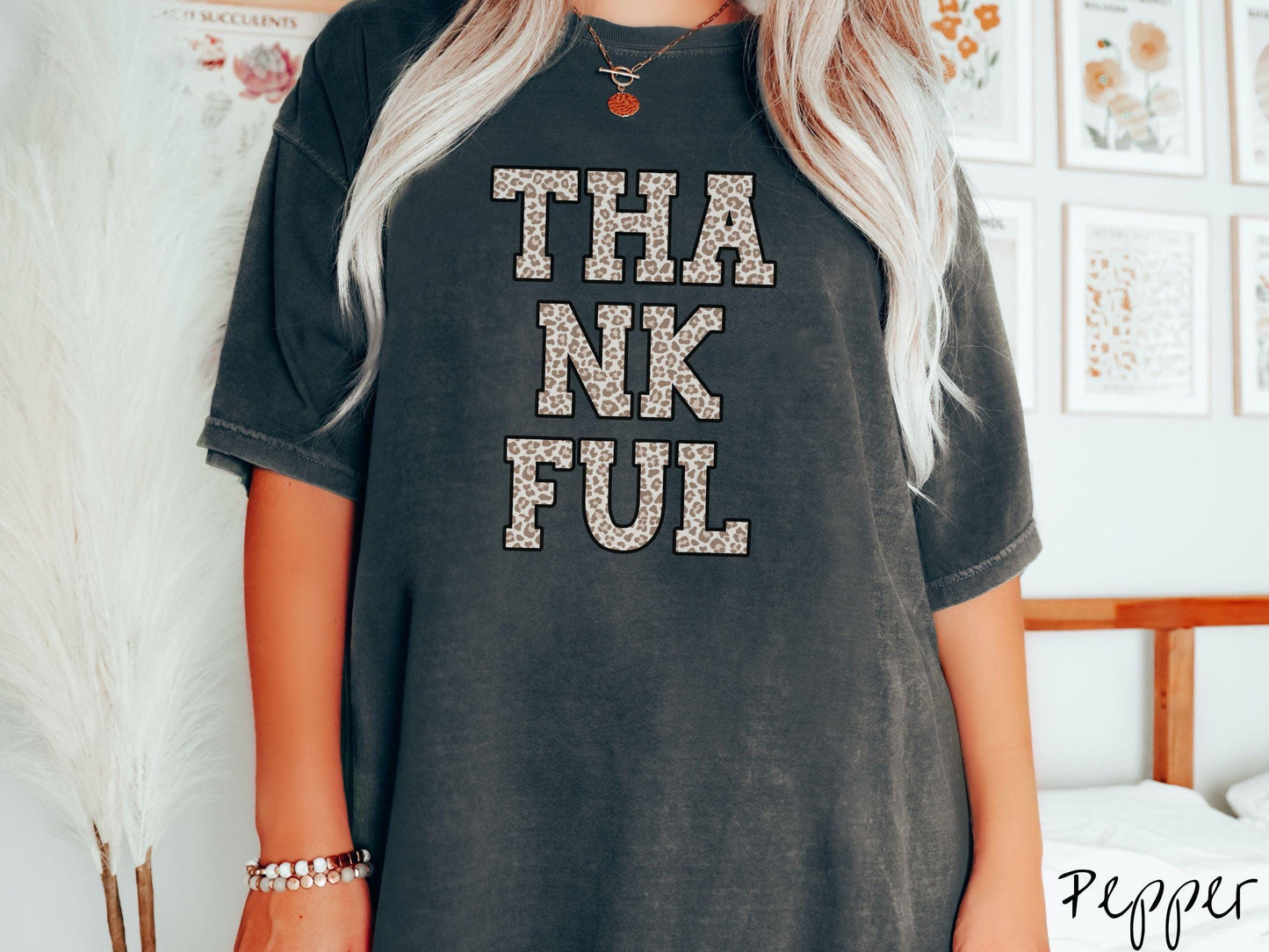 A woman wearing a cute, vintage pepper colored Comfort Colors T-shirt with the text THANKFUL in capital letters stacked in three rows across the front. The letters are in ivory, light brown, and dark brown colored leopard print font.